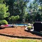 Here is an after shot of the finished landscaping project we completed in Manchester NH. The image shows a clean and freshly mulched garden bed to the left of a patio in front of a pool.