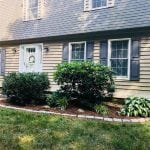 This is an image of a recent landscaping project we finished in Manchester NH. This image shows the front left corner of the home with a clean garden bed along the front of the home. There are light gray bricks surrounding the garden bed.