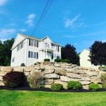 This is a wide shot of the front of a Hooksett NH home where we complete lawn care work. This home owner has many stone retaining walls in the front yard where we added fresh mulch to the garden beds.