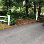 Check out the before shot of what our Manchester NH landscaping service recently completed. The image shows the end of the driveway facing the road. The image shows an overgrown garden on the left side of the driveway.